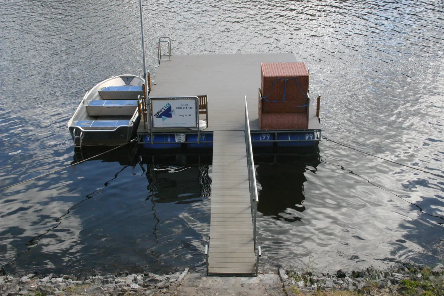 Fischerei-Pächtergemeinschaft Rursee e.V. - Nachhaltige Sportfischerei und Umweltschutz - Ein kleines Boot, das an einem hölzernen Schwimmsteg auf einem See festgemacht ist.